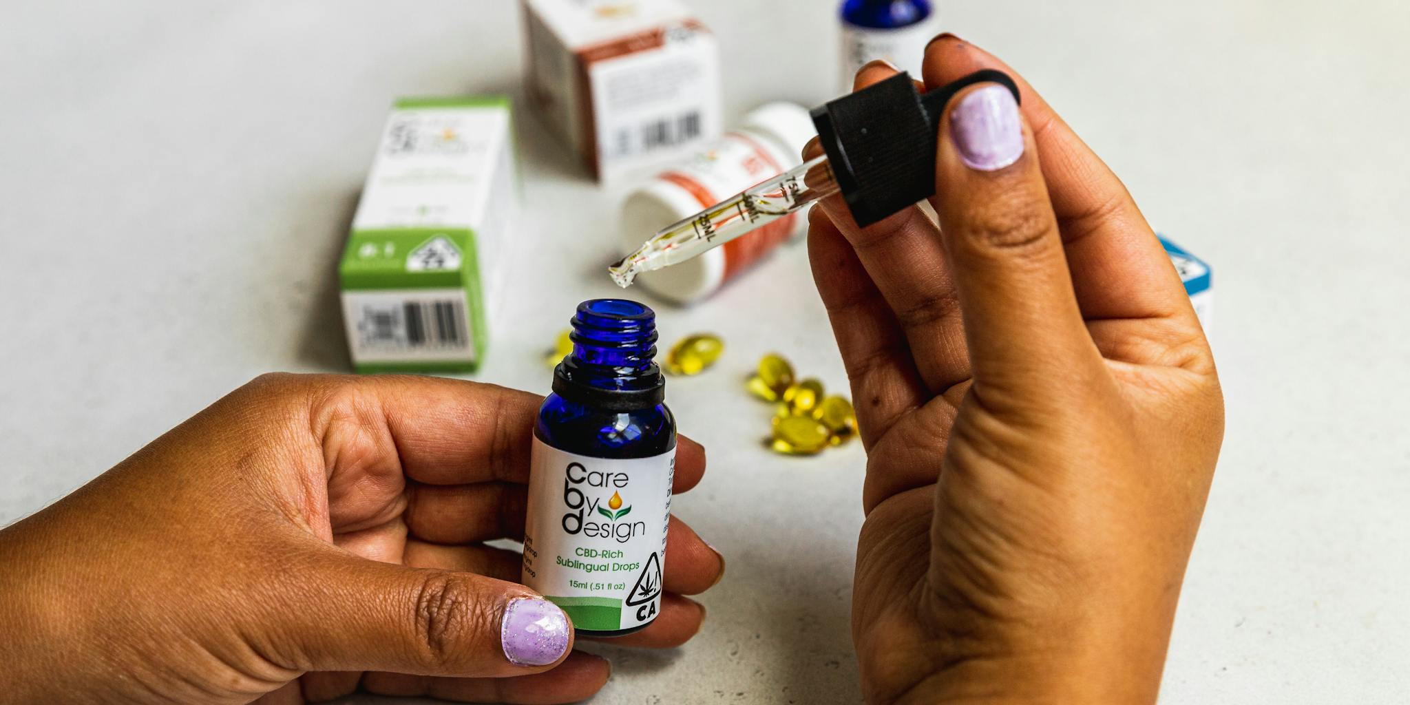 A detailed image showing hands using a dropper to handle CBD oil with packaging in the background.